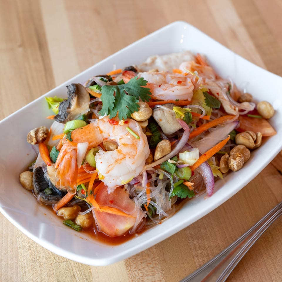 Close-up of a vibrant Thai glass noodle salad with shrimp, vegetables, and peanuts in a white bowl.