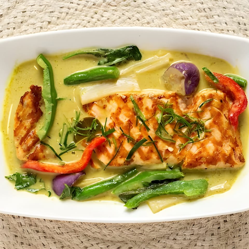 Grilled salmon in green curry with red bell peppers, green beans, and purple eggplant in a white dish.