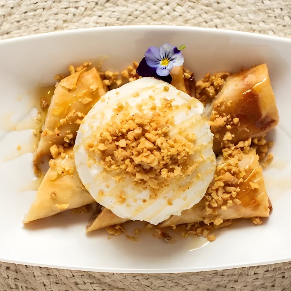 Fried banana spring rolls with vanilla ice cream, chopped nuts, honey, and a purple edible flower.
