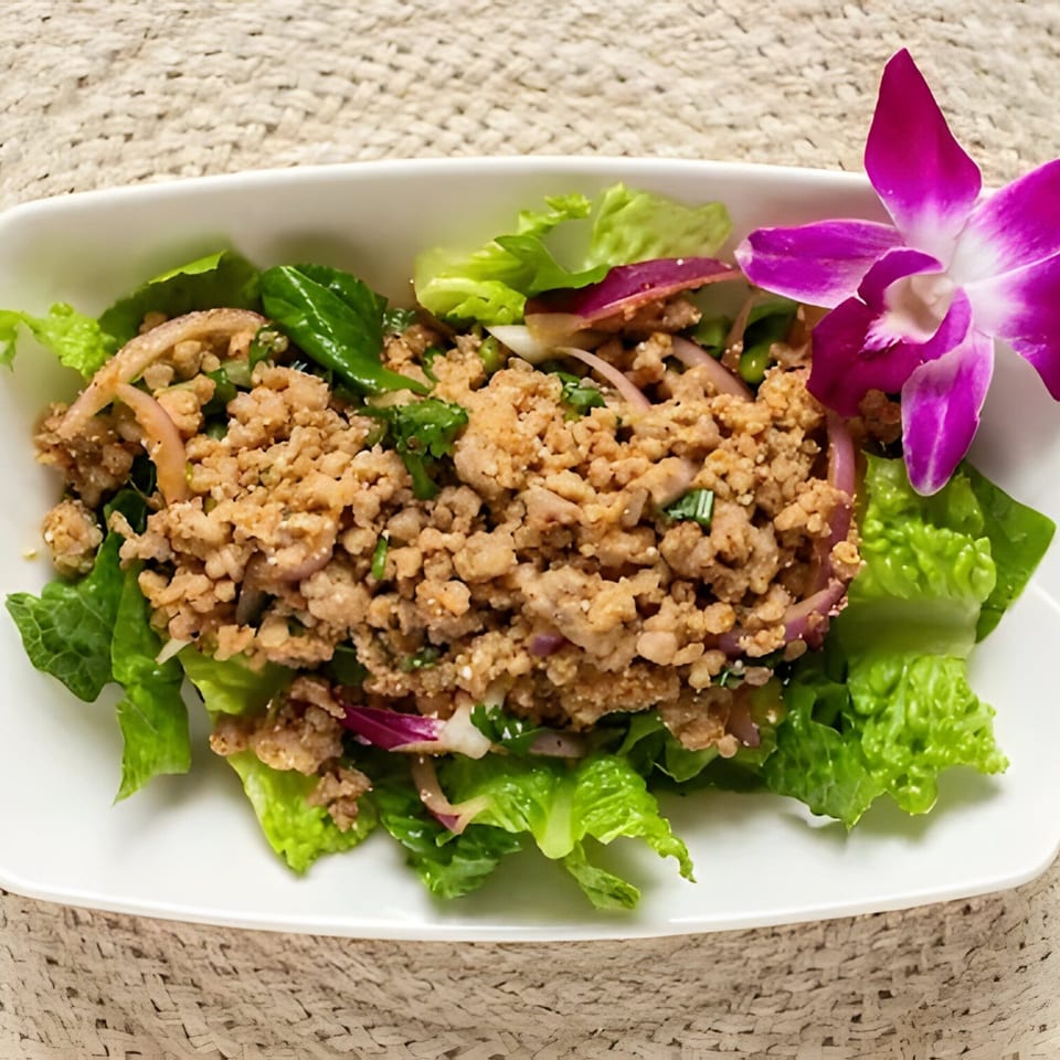 Thai Larb Gai, a minced chicken salad with fresh herbs and red onion, garnished with an orchid.