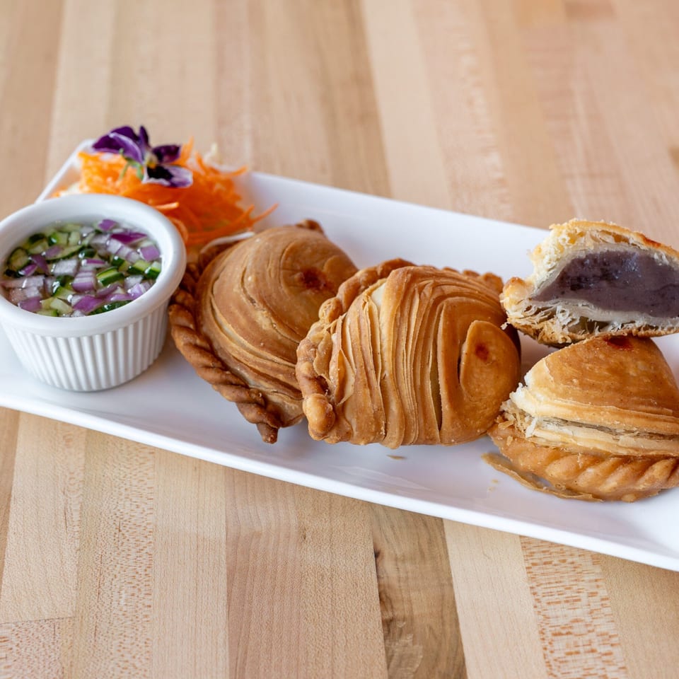 Thai curry puffs with a side of dipping sauce and shredded carrots on a white plate.