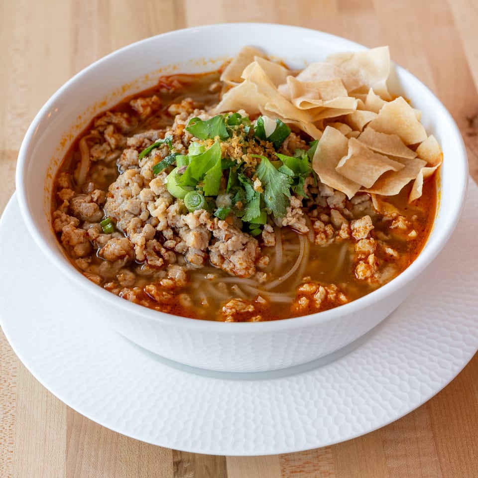 A bowl of M Thai Kitchen's spicy Thai noodle soup with minced pork, herbs, and crispy wontons.