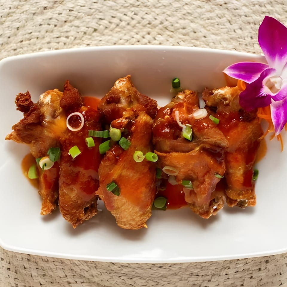 Crispy Thai chicken wings with sweet chili sauce, green onions, and a purple orchid garnish.