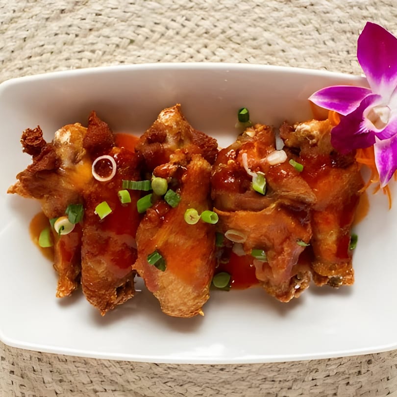 Crispy Thai chicken wings with sweet chili sauce, green onions, and a purple orchid garnish.