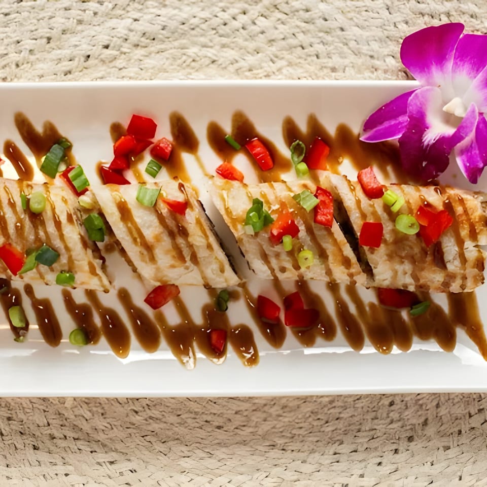 Sliced Thai appetizer drizzled with sauce, topped with red peppers and green onions, garnished with an orchid.